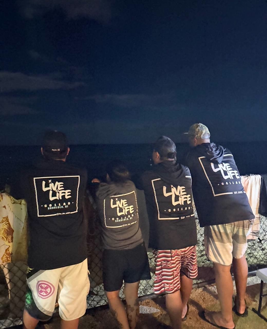 Four people in Live Life Collab tees on the seawall after dark